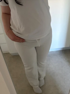 Vita mjukisbyxor med dragsko - Säljer ett par vita mjukisbyxor med raka ben och dragsko i midjan. Byxorna har en enkel och stilren design, perfekta för en avslappnad look. Tillverkade i mjukt material som känns skönt mot huden.