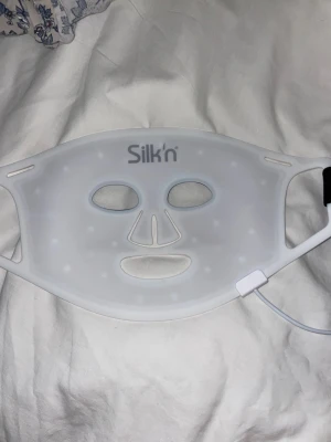 Silk'n LED ansiktsmask - LED ansiktsmask från Silk'n i vit silikon med utskärningar för ögon, näsa och mun. Masken har inbyggda LED-lampor och ansluts med kabel för hudvård och behandling av ansiktet. Modellen heter 	Silk'n Facial LED Mask 100 LEDS. Säljer då jag fått en ny från ett annat märke, den är som ny
