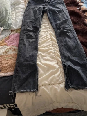 Svarta jeans med råa kanter - Säljer ett par svarta jeans i denim med raka ben och råa, fransiga benslut. Jeansen har klassisk femficksdesign och är perfekta för en avslappnad och trendig look. Märke och storlek är okänt.