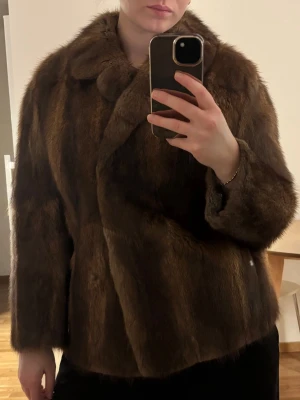 Mörkbrun pälsjacka med krage - Säljer en snygg mörkbrun pälsjacka med klassisk krage och rak passform. Jackan har långa ärmar och stängs framtill. Köpt secondhand så vet ej märke. 