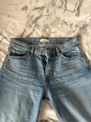 Blå raka jeans från Gina tricot  - Säljer ett par klassiska blå raka jeans från gina tricot. Jeansen har fem fickor, bälteshällor och stängs med knapp och dragkedja. Tillverkade i slitstark denim med snygg tvättad look och kopparfärgade nitar. Perfekta till en avslappnad stil.