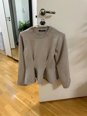 Beige stickad peplumtröja från Gina tricot  - Säljer en beige stickad tröja från Gina tricot  med peplumformad nederkant och rund halsringning. Tröjan har långa ärmar och är perfekt för dig som gillar en enkel men snygg stil. Passar till många olika outfits.