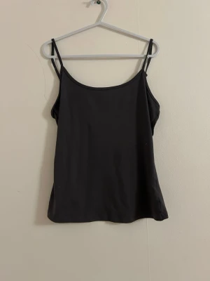 Grå  enkel linnetopp - Säljer en grå  linnetopp med smala axelband och rundad halsringning. Toppen har en clean och minimalistisk look, perfekt att styla lager på lager eller bära som den är. Materialet känns mjukt och följsamt mot huden.