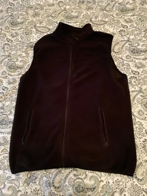 Svart fleeceväst med dragkedja - En enkel och stilren svart fleeceväst med hel dragkedja framtill och två fickor med dragkedja. Västen har hög krage och är perfekt att slänga över en tröja för extra värme. Passar till många olika outfits och är riktigt bekväm.