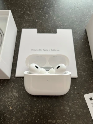 Apple AirPods Pro trådlösa hörlurar - Säljer ett par vita Apple AirPods Pro med laddningsetui. Hörlurarna har en stilren och kompakt design med silikonproppar för bra passform. Perfekta för musik, samtal och träning. Levereras med originalförpackning och laddkabel.