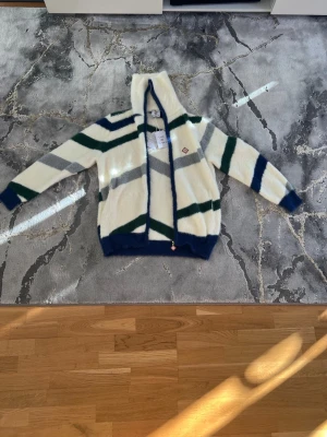 Casablanca Cardigan ullmix - Säljer en fluffig hoodie från Casablanca i mjuk ullmix. Den är vit med breda ränder i mörkgrönt, marinblått och grått. Hoodien har dragkedja framtill, ribbade muddar och en stor huva. Perfekt för dig som gillar en avslappnad och trendig stil.  Pris kan ev disskuteras, enbart seriösa köpare. Kan vid efterfrågan även mötas i Stockholm. Allt är i nyskick