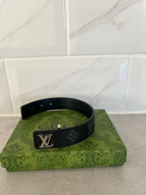 Svart armband - Snyggt svart armband från LV i läder med klassiskt monogrammönster och en silverfärgad LV-logga framtill. Armbandet har justerbar storlek och en stilren design som passar perfekt till din outfit.  Pris kan ev disskuteras, enbart seriösa köpare. Kan vid efterfrågan även mötas i Stockholm. Allt är i nyskick