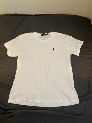 Vit t-shirt från Polo Ralph Lauren - Klassisk vit t-shirt från Polo Ralph Lauren med rund halsringning och korta ärmar. Liten broderad logga i svart på bröstet ger en clean och stilren look. Tillverkad i mjuk bomull för maximal komfort.