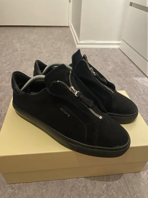 Axel arigato - Stilrena svarta sneakers från Axel Arigato i mocka med cool dragkedja framtill istället för klassiska snören.  Denna modell säljs inte längre, så dom är svåra att få tag på. Skorna är i 7-10 skick bara att på högra skorn så har tråden låsnat men de finns inga konstigheter med dom det är enkelt att sy ihop, Box dustbag och klistermärken kommer, hör bara av dig vid minsta fundering. (Ops! metalgrejen följer inte med)