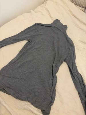 Grå polotröja i tunn bomull från H&M  - Säljer en enkel och stilren grå polotröja med lång ärm. Tröjan är tillverkad i ett tunt och mjukt bomullsmaterial, perfekt för lager på lager. Polokragen ger en clean look och passar till många olika outfits. Använts fåtal gånger och är ifrån H&M 