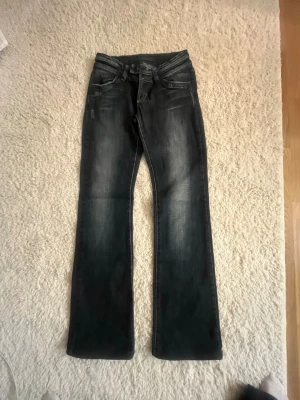 Mörkblå bootcut jeans med slitningar - Säljer ett par mörkblå bootcut jeans med snygga slitningar och tvättade detaljer. Jeansen har klassisk femficksmodell, dubbla knappar i midjan och dragkedja. Materialet är denim i bomull med lite stretch för extra komfort. Jätte låg midjade.