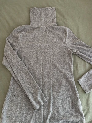 Grå polotröja i mjukt stickat tyg - Säljer en enkel och stilren grå stickad polotröja med lång ärm och hög krage. Tröjan är i ett mjukt och stretchigt material som sitter skönt på kroppen. Perfekt att matcha med jeans eller kjol för en clean look.