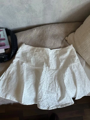 Vit kort kjol  - Söt vit kort kjol med broderade blommor och hålmönster. Kjolen har en lätt utsvängd form och är gjord i ett mjukt bomullstyg. Perfekt till sommaren. Från H&M storlek 42💕