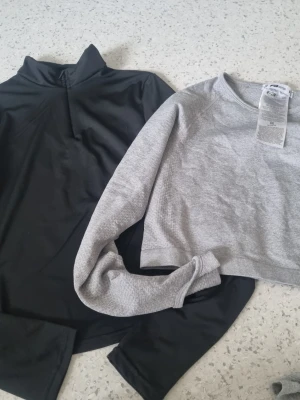  2 st Grå croppad sweatshirt & svart tröja - Säljer en grå croppad sweatshirt med rund hals och ribbade muddar samt en svart långärmad tröja med hög krage. Perfekta basplagg för en avslappnad och trendig stil.