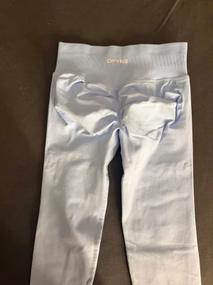 DFYNE Seamless Scrunch Leggings - Ljusblå - Storlek XS - Säljer mina superfina DFYNE seamless leggings i en fantastisk ljusblå färg. Storlek Extra Small (XS). DFYNE är kända för sin otroliga komfort och kvalitet som håller passformen genom hela passet. De har den populära "scrunch butt"-designen (som syns tydligt på bild 1 och 3) som ger en fantastisk form. Materialet är mjukt, stretchigt och helt knäböjssäkert (squat-proof). Den höga midjan sitter på plats utan att rulla ner. Tightsen är i mycket fint skick och säljes då jag rensar ut i garderoben. 