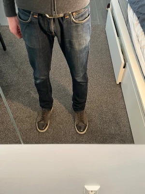Mörkblå Nudie raka jeans - Säljer ett par mörkblå jeans med klassisk rak passform och fem fickor. Jeansen har kontrastsömmar och en tidlös look som passar till det mesta. Tillverkade i slitstarkt denimtyg, perfekta för dig som gillar en enkel och clean stil.W33 L32