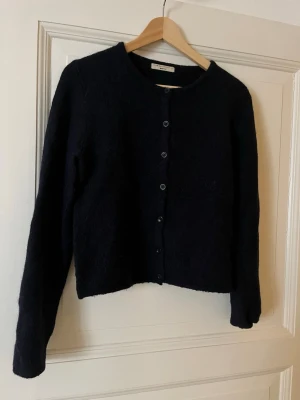 Marinblå kofta från Gina Tricot - Mysig  kofta från Gina Tricot i storlek M. Koftan har rund halsringning, knappar framtill och är tillverkad i ett fluffigt material som känns riktigt skönt. Perfekt att slänga på sig när det är kyligt ute.