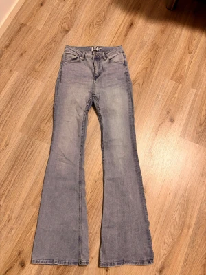 Ljusblå utsvängda jeans  - Säljer ett par ljusblå jeans med utsvängda ben. Jeansen har hög midja och är tillverkade i ett mjukt denimtyg. Perfekta för dig som gillar retrovibbar och vill ha en avslappnad men trendig look.