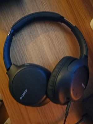 Svarta over-ear hörlurar från Sony - Stilrena svarta over-ear hörlurar från Sony med vadderad bygel och mjuka öronkuddar. Sladdanslutning och diskret Sony-logga på kåporna. Perfekta för musik, gaming eller poddar.