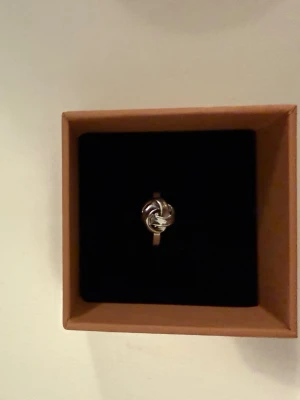 Snygg silverfärgad knutring - Stilren ring i silverfärg med en unik knutdesign framtill. Ringen har en slät, blank yta och känns både modern och tidlös. Perfekt accessoar för dig som gillar minimalistiska smycken med en twist.