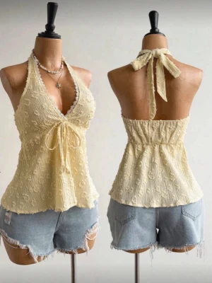 Gul spetsdetaljerad halterneck topp - Söt ljusgul halterneck topp med spetskant och knyt framtill. Toppen har ett diskret blommönster i tyget och är tillverkad i ett lätt, luftigt material. Perfekt för varma dagar och ger en romantisk vibe.