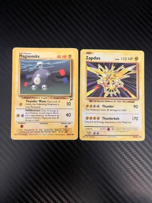 Pokémonkort Magnemite & Zapdos - Två klassiska Pokémonkort: Magnemite och Zapdos från den ursprungliga serien. Magnemite har gul ram och motiv med metallisk kropp, medan Zapdos har ett gult, elektriskt motiv. Båda korten har den ikoniska blå baksidan med Pokéboll. Perfekt för samlare eller nostalgiker. Båda är i bra skick. Svarar snabbt👍🏽