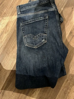 Replay jeans - Säljer ett par mörkblå jeans med raka ben och slitningar framtill för en cool, avslappnad look. Jeansen har klassiska fem fickor och kontrastsömmar. Perfekta för dig som gillar en trendig stil.