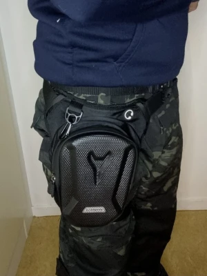 Leg Bag - MC - benväska - tactical bag - Hard shell-lastar mycket mer än du tror - Svart benväska med hårt skal i Kolfiber och justerbara remmar för att fästas runt midjan och låret och har en robust konstruktion.  Sitter ordentligt när du kör.  Finns hjälmar, mc handskar, masker         snabb kontakt. Paketpris möjligt.  Ny i paket