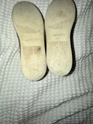 Bruna Lanvin sneakers i läder - Snygga bruna sneakers från Lanvin med ovandel i läder och klassisk rund tå. Skorna har svarta skosnören och vit sula med Lanvin-logga undertill. Perfekta för dig som gillar stilrena och exklusiva sneakers. Skorna är ganska slitna.