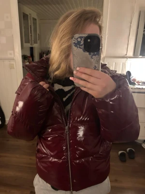 Jacka  - Säljer en vinröd pufferjacka med glansig finish och huva. Jackan har dragkedja framtill och är vadderad för extra värme. Perfekt för kalla dagar och har en modern, boxig passform. Snygg och trendig jacka som håller dig varm hela vintern.