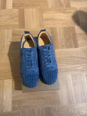 Blå sneakers med nitar - Unika blå sneakers med matchande blå skosnören och coola nitar över hela tån. Skorna har en låg profil och är tillverkade i mockaliknande material. Insidan är beige och designen är riktigt edgy och trendig.