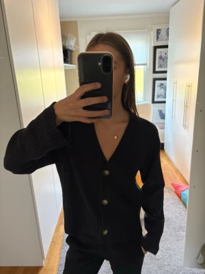 Svart ribbad kofta med knappar - Svart kofta med v-ringning och stora knappar framtill. 