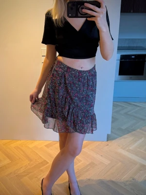 Blommig volangkjol i chiffong - Söt kortkjol med blommigt mönster. Kjolen har volangkant nertill och är gjord i ett lätt, luftigt material som ger en flowy känsla. Perfekt för vår och sommar