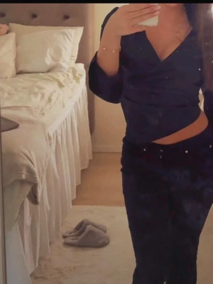 Svart omlottopp med lång ärm - Snygg svart omlottopp med lång ärm och v-ringning. Toppen har en croppad passform och är gjord i ett glansigt polyestermaterial som ger en elegant look. Perfekt att styla med höga jeans eller kjol.