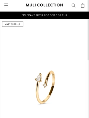 Guldfärgad ring med kristaller - Snygg guldfärgad ring från Muli Collection med öppen design och två kristaller, varav en är droppformad och den andra rund. Ringen har en elegant och modern look, perfekt för att ge din stil en extra touch. Materialet är metall med kristalldetaljer.