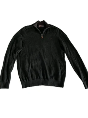 Mörkgrön halvzip tröja från Morris - Mörkgrön stickad tröja från Morris i storlek L med halv dragkedja och liten broderad logga på bröstet. Tröjan har ribbade muddar vid ärmslut och nederkant samt en klassisk passform. Perfekt för lager på lager och stilren look.