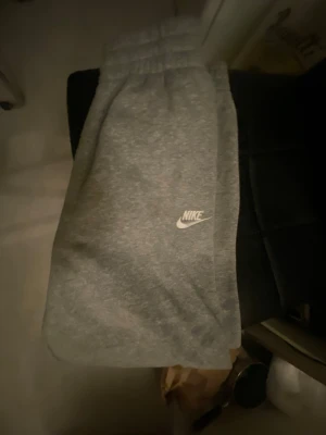 Gråa mjukisbyxor från Nike - Säljer ett par klassiska gråa mjukisbyxor från Nike med vit logga på benet. Byxorna har resår i midjan och vid bensluten samt sidofickor. Perfekta för chill dagar eller träning. Tillverkade i mjukt och bekvämt material.