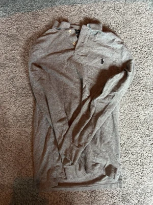 Grå långärmad polotopp Polo Ralph Lauren - Säljer nu denna riktigt snygga Polo Ralp Lauren tröja som är i topp skick - bara använd ett fåtal gånger - storlek S - hör av er vid prisförslag!