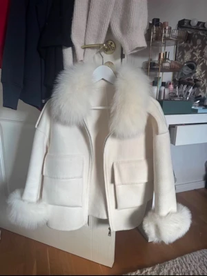Vit pälsjacka med stor krage - Snygg vit pälsjacka med stor fluffig fuskpälskrage och två stora fickor framtill. Jackan har rak passform och dragkedja. Ordinariepris:3200 från bellojackets. Perfekt för dig som vill ha en trendig och varm look i vinter eller hösten