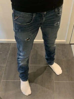 Replay Anbass Jeans aged 5 years - Säljer denna tvärfeta Anbass modellen av replay som är aged 5 years för att ge den snygga fasen och looken. Byxorna är storlek 29/32, riktigt schyssta med slitningar som del av designen. Skriv gärna vid intresse