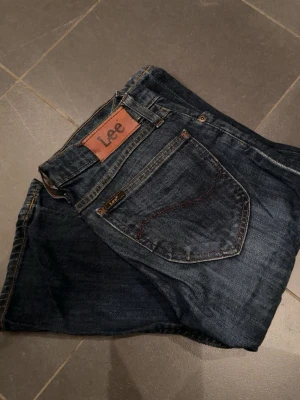 Mörkblå lågmidjade Lee jeans med bootcut - Säljer ett par mörkblå lågmidjade jeans från Lee med klassisk femficksmodell med en mindre bootcut. Jeansen har snygga kontrastsömmar och en brun läderpatch med Lee-loggan bak i midjan. Perfekta för en avslappnad och stilren look. Skriv privat för fler bilder🌸