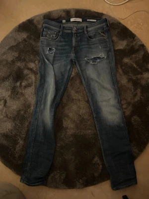 Blå slitna jeans från Replay - Säljer ett par blå jeans från Replay med slitningar och hål på låret. De är fina i skicket kom privat för mer info 