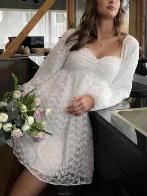 Vit studentklänning - Supersöt vit kortklänning med blommigt spetsmönster och långa puffärmar. Säljer min studentklänning från NAKD då den inte kommer komma till användning igen🥰