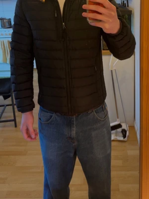 Svart pufferjacka från Parajumpers - Säljer en svart pufferjacka från Parajumpers med quiltad design och dragkedja framtill. Jackan har två sidofickor med dragkedja och en patch med Parajumpers-logga på vänster ärm. Perfekt för kalla dagar och riktigt snygg till jeans.Storlek Y-L men sitter som en vanligt M