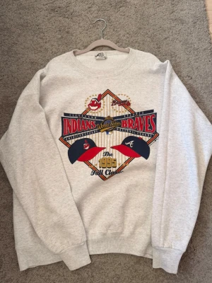 Vintage MLB sweatshirt 1995 - Cool grå sweatshirt med stort färgglatt tryck från 1995 World Series mellan Cleveland Indians och Atlanta Braves. Tröjan har rund hals och långa ärmar, perfekt för dig som gillar vintage sportmode och unika prints.