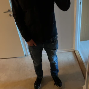 Blå replay jeans - Säljer ett par blå jeans med slitningar och hål på låret för en cool och avslappnad look. Jeansen har en rak passform och klassisk femficksdesign. Perfekta för dig som gillar streetstyle och vill ha ett par jeans med attityd.