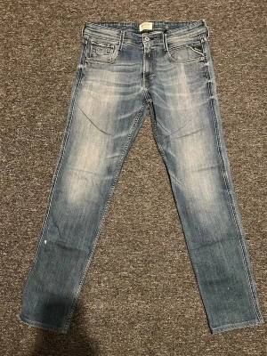 Replay anbass jeans - Snygga blå slim fit jeans från replay med slitningar och ljusare partier framtill. Klassisk femficksmodell med detaljerade sömmar på bakfickan och små röda accenter. Perfekta för en avslappnad och trendig look.