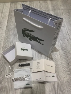 Lacoste Metropole armband i silver - Snyggt Metropole armband från Lacoste i silverfärgat rostfritt stål. Armbandet har en modern, länkad design med diskret Lacoste-logga och levereras i originalförpackning med påse och certifikat. Perfekt accessoar för dig som gillar stilrena detaljer.