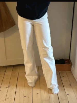 Vita raka jeans med rå kant - Säljer ett par vita jeans med rak passform och råa, fransiga benslut. Jeansen har hög midja och klassisk femficksdesign. Perfekta för en clean och trendig look. Materialet ser ut att vara bomull med lite stretch.