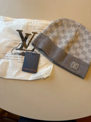 Grå mössa med rutmönster - Snygg grå mössa med klassiskt rutmönster och vikt kant. logga sitter framtill på kanten. Tillverkad i mjukt stickat material. Perfekt accessoar för att lyfta din outfit.